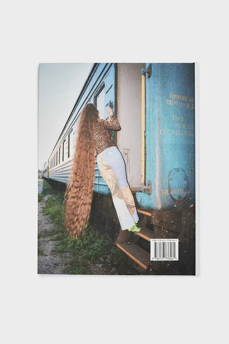 Woman with long hair in leopard print top and white pants climbing blue train carriage